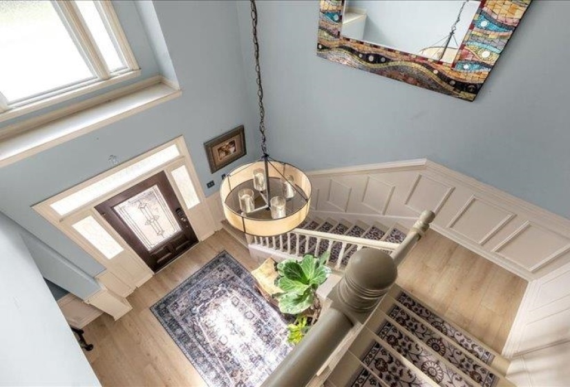 Two-story foyer featuring light wood-finish flooring, a decorative front door with transom and sidelights, an overhead chandelier, and wainscoting along the staircase