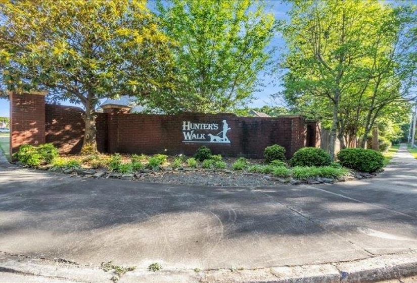 Brick entry monument featuring "Hunter's Walk" signage, integrated landscaping, and mature trees