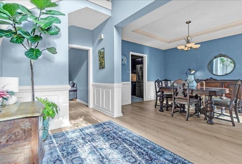 Formal dining area featuring light wood-finish flooring, wainscoting, and a tray ceiling with a central chandelier