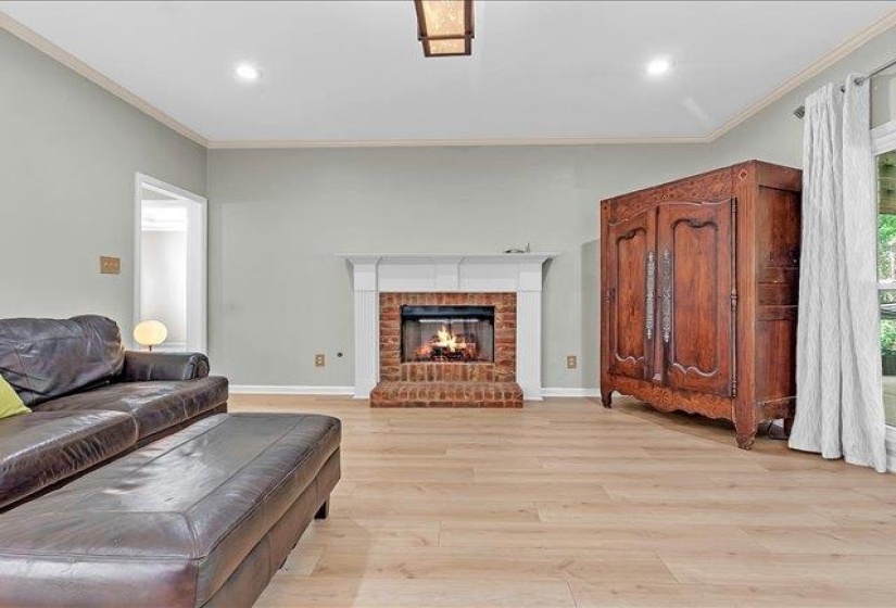 Living area featuring a brick fireplace with a white mantel, light wood-finish flooring, recessed lighting, and crown molding