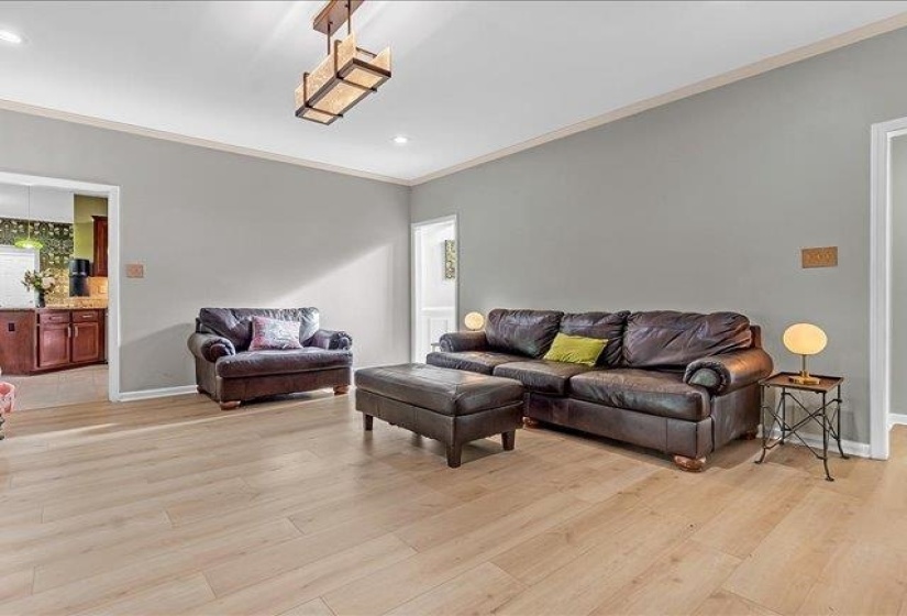Spacious living area featuring light wood-finish flooring, neutral gray walls, and white crown molding
