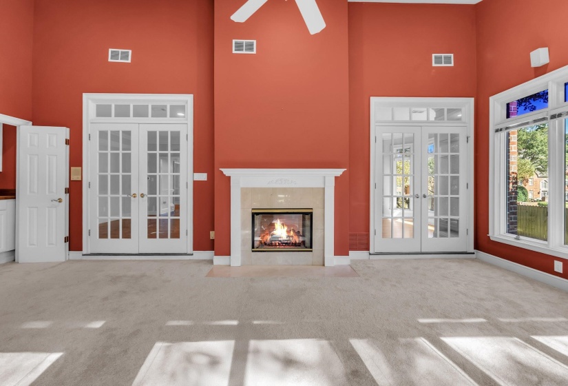 Spacious living area featuring a central fireplace with an ornate mantel, two sets of French doors with transom windows, and multiple windows providing ample natural light