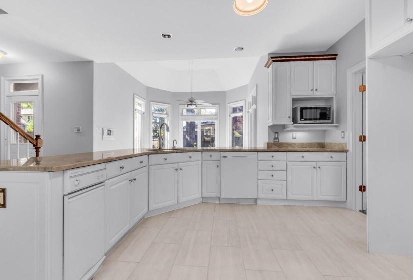 Kitchen featuring light wood-finish flooring, white cabinetry, integrated appliances, and a bay window with a sink