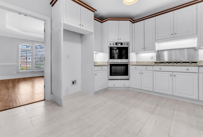 Kitchen featuring white shaker-style cabinetry with crown molding, stainless steel double wall ovens, a matching gas cooktop with stainless steel backsplash, light-toned stone countertops, and plank tile flooring