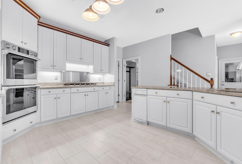 Spacious kitchen featuring white cabinetry with brushed nickel hardware, light-toned countertops, a built-in double oven, and a gas cooktop