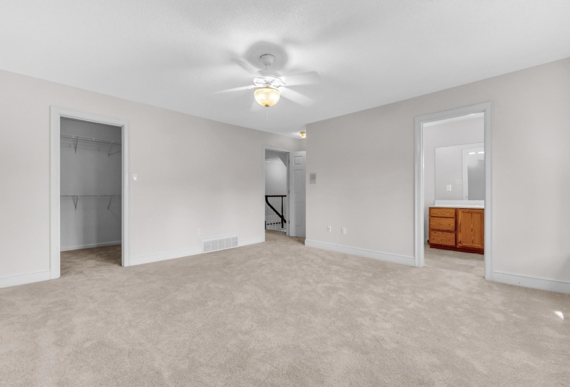 Carpeted room with a ceiling fan, featuring a closet with wire shelving and an entry to a bathroom with a wood vanity