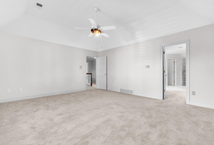 Spacious room featuring vaulted ceilings, light-colored carpeting, and a ceiling fan with integrated lighting