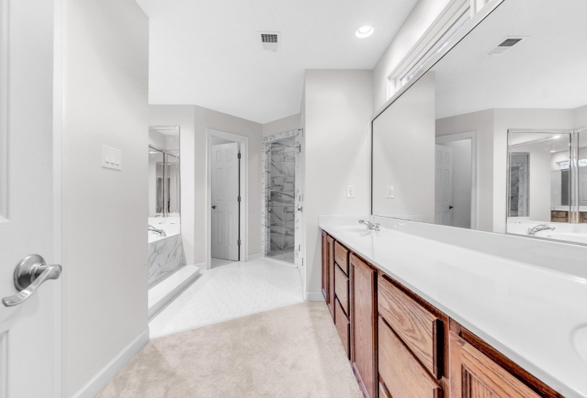 Bathroom featuring a double vanity with integrated sinks, a lengthy wall mirror, recessed lighting, and wood-finish cabinetry