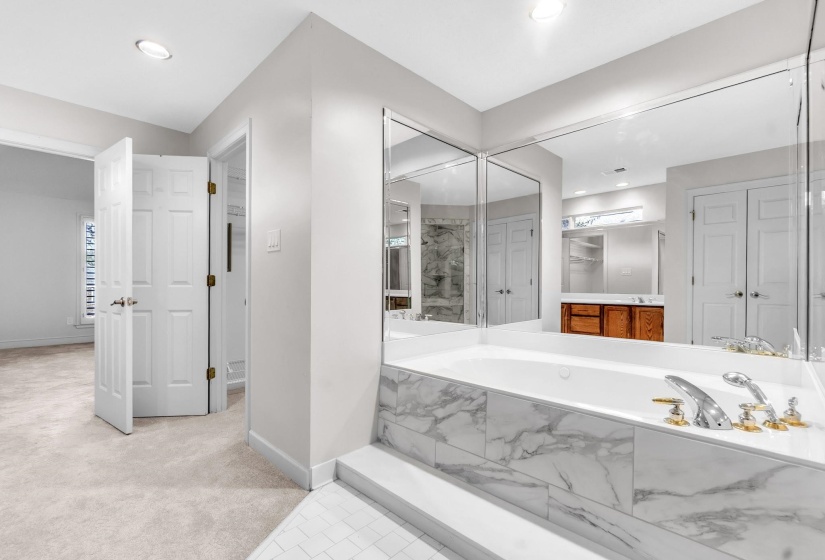 Soaking tub with marble-look surround, mirrored wall, recessed lighting, and carpeted flooring