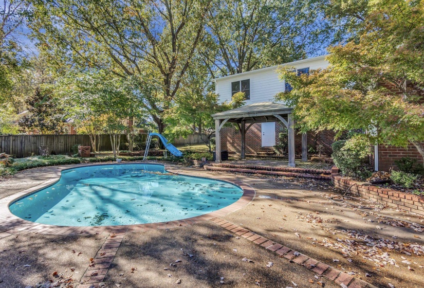 Rear exterior featuring a freeform swimming pool with concrete decking and brick accents