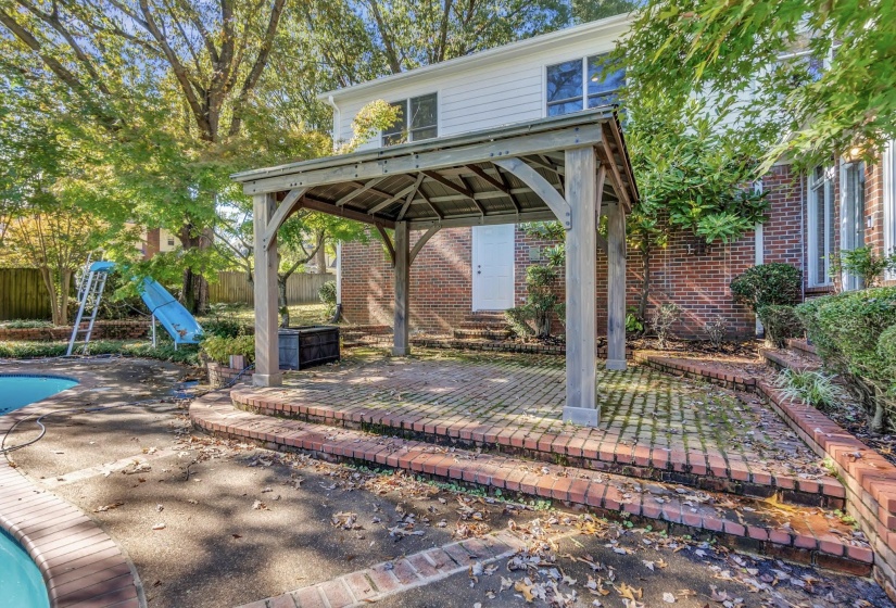 Spacious outdoor patio area featuring a wooden gazebo with a shingled roof, brick paver flooring, and curved brick steps