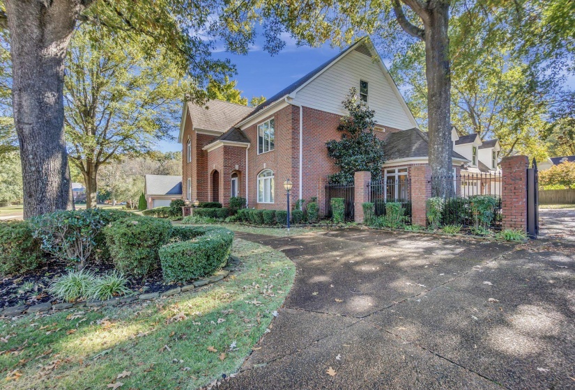 Brick exterior residence featuring a gabled roofline, mature trees, and a paved driveway