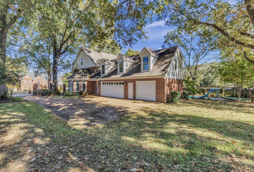 Two-story brick residence featuring multiple dormer windows, an attached three-car garage, and mature trees on a spacious lot