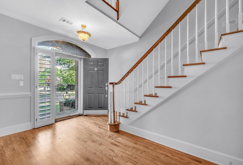 Foyer featuring wood-finish flooring, a grand staircase with wood handrails, a transom window, and a chandelier