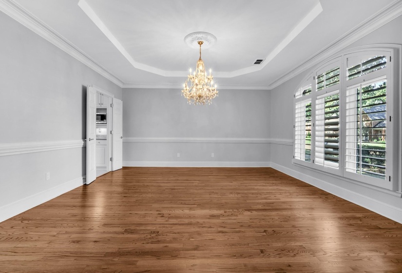 Spacious room featuring wood-finish flooring, an ornate crystal chandelier, and a tray ceiling