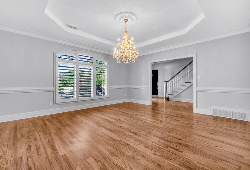 Spacious room featuring wood-finish flooring, a tray ceiling with a chandelier, wainscoting, and an arched window with plantation shutters