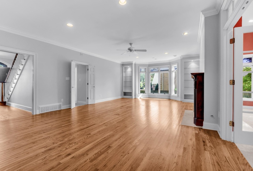 Spacious living area featuring polished wood flooring, a fireplace with a detailed wood mantel, multiple built-in shelving units, and a bay window configuration