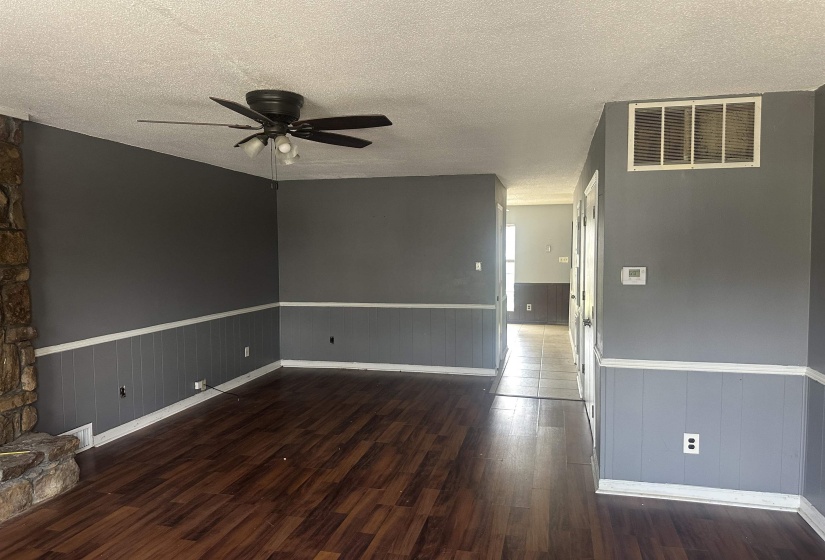 Spacious interior with wood-finish flooring, a stone-clad fireplace, and paneling with chair rail trim