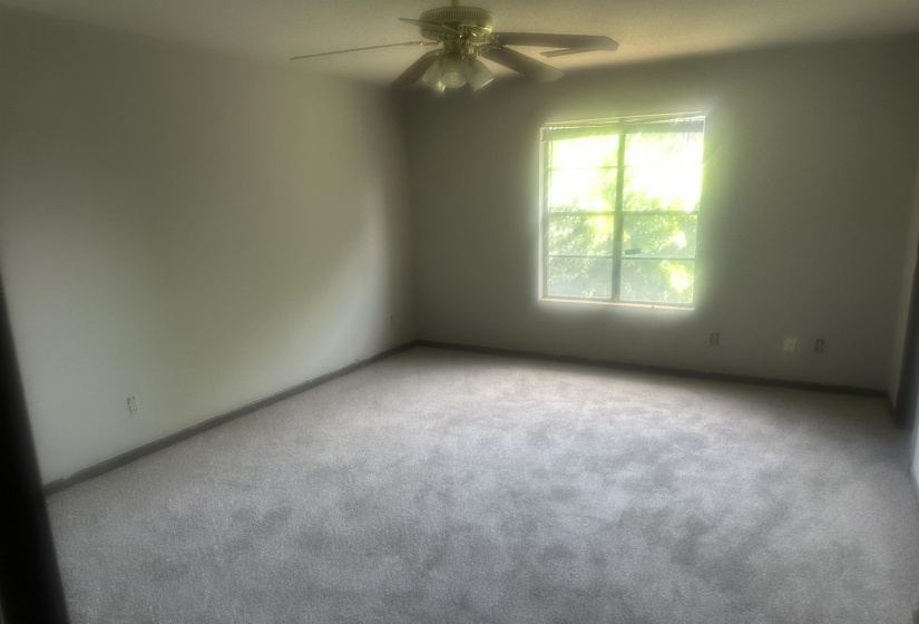 Spacious room featuring light gray carpeting, a large window, and a ceiling fan