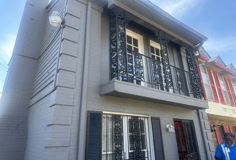 Gray brick and siding exterior featuring a second-story balcony with intricate black wrought iron railings
