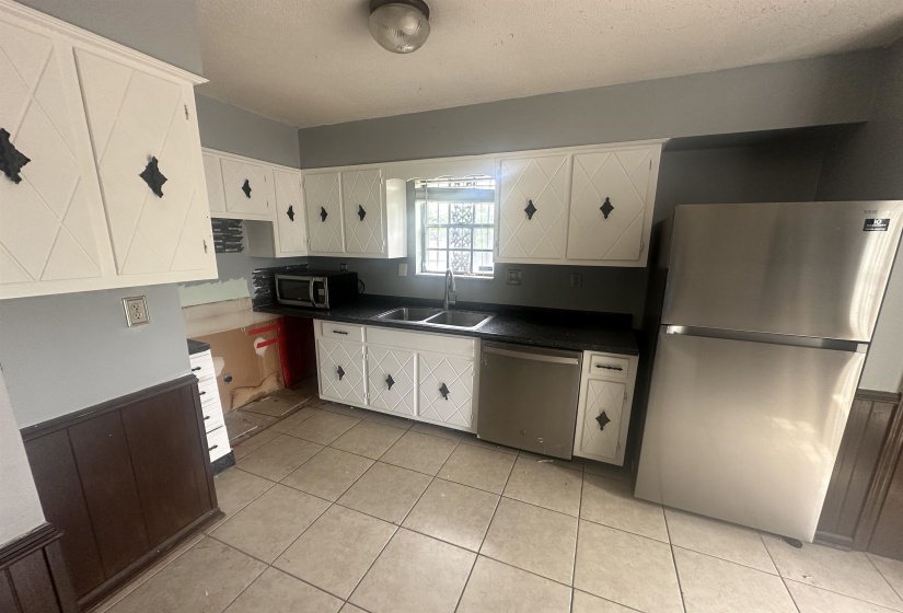 Kitchen featuring white cabinetry with decorative diamond-pattern panels, dark countertops, and a stainless steel refrigerator