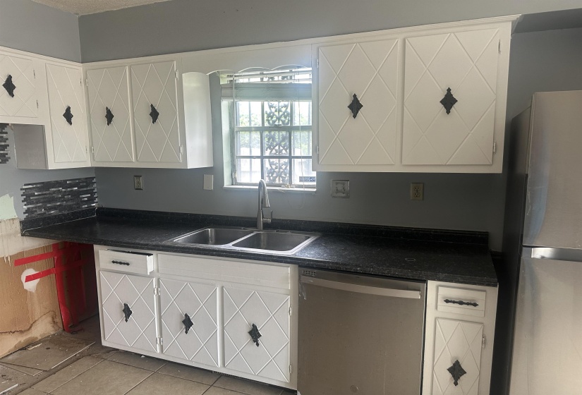 Kitchen featuring white cabinetry with decorative diamond paneling, dark speckled countertops, a stainless steel double basin sink with a high-arc faucet, and tiled flooring
