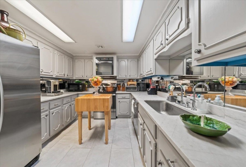 Kitchen featuring gray cabinetry, stainless steel appliances, light tile patterned floors, and light stone counters