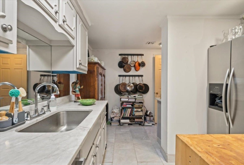 Kitchen featuring stainless steel fridge with ice dispenser, white cabinetry, ornamental molding, light stone countertops, and light tile patterned flooring