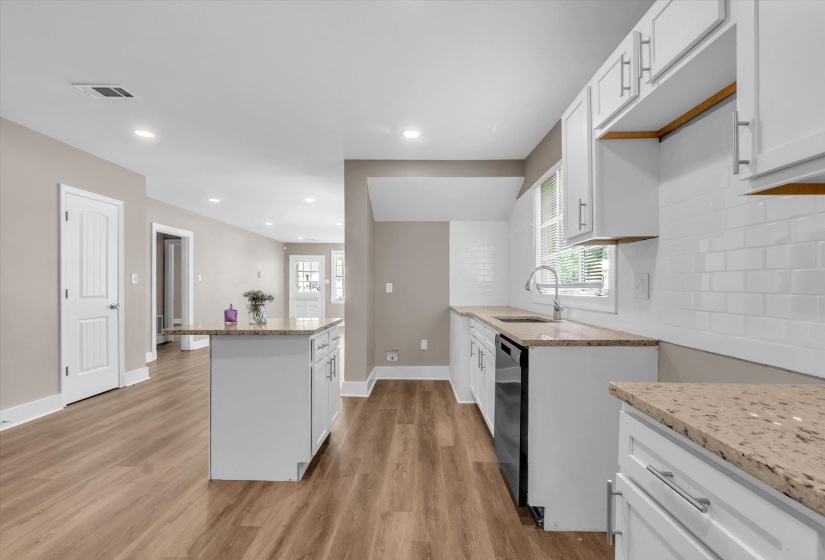 Kitchen featuring an island with stone-finish countertop, white shaker cabinetry, stainless steel sink, subway tile backsplash, and wood-finish flooring