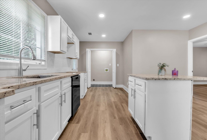 Modern kitchen with light wood-finish flooring, white cabinetry, and light-toned granite countertops
