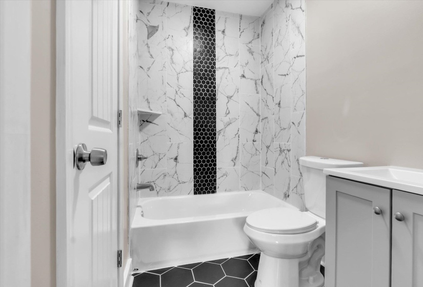 Bathroom featuring a white bathtub, black hexagonal floor tiles, and a tiled shower surround with white marble-patterned tiles and a black hexagonal accent stripe