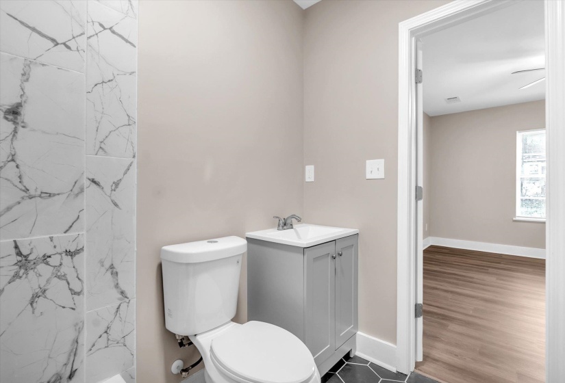 Bathroom featuring large-format white tile with gray veining, a white toilet, and a gray vanity with an integrated sink