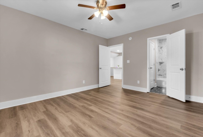 Spacious room featuring wood-finish flooring, neutral-toned walls, and a ceiling fan with integrated lighting