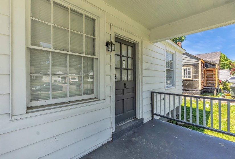 Front porch featuring white siding, a dark paneled door with glass inserts, a multi-pane window, and a dark porch railing