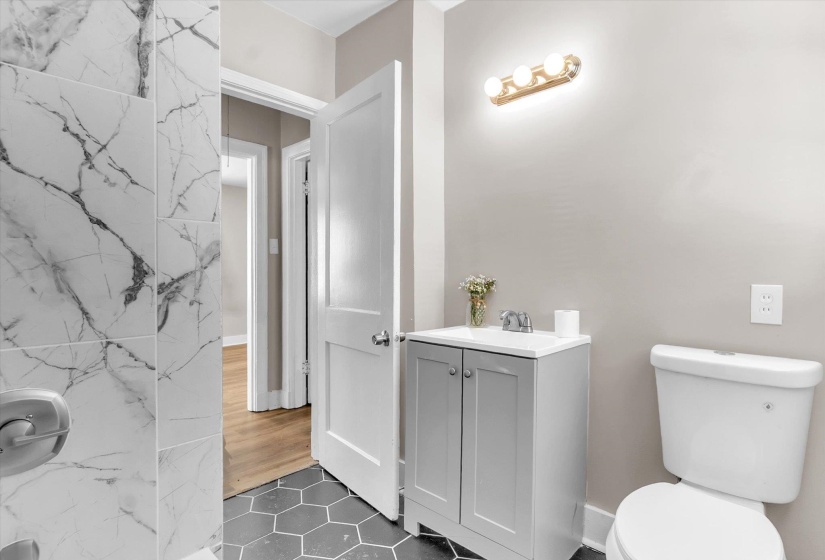 Bathroom featuring hexagon floor tile, a white vanity with gray cabinetry, a wall-mounted light fixture, and white wall tile with gray veining