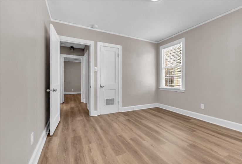 Room featuring wood-finish flooring, neutral wall paint, white trim, a single window with blinds, and white interior doors