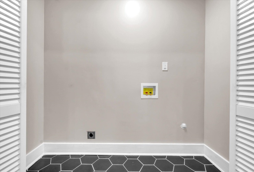 Dedicated laundry area featuring black hexagonal tile flooring and white baseboards