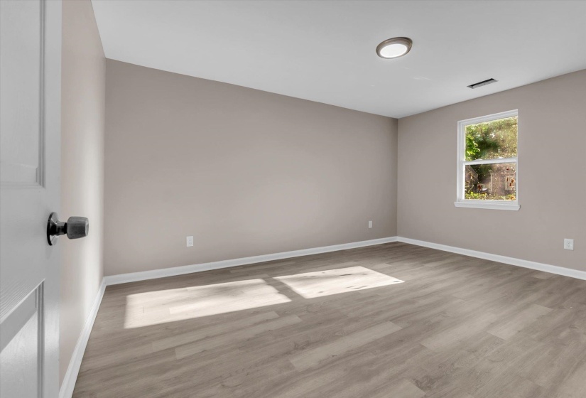 Neutral-toned room featuring light wood-finish flooring, white baseboards, a double-hung window, and a ceiling-mounted flush light fixture