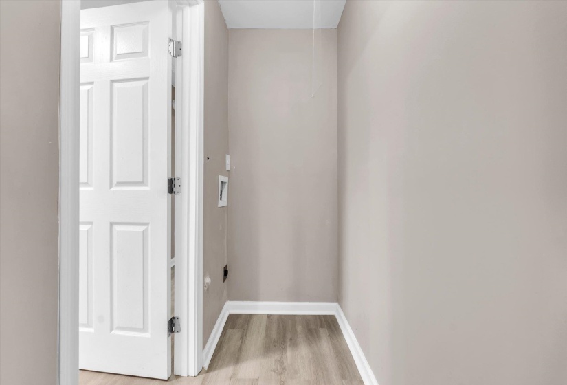 Dedicated utility area featuring wood-finish flooring, light neutral wall tones, and white baseboards