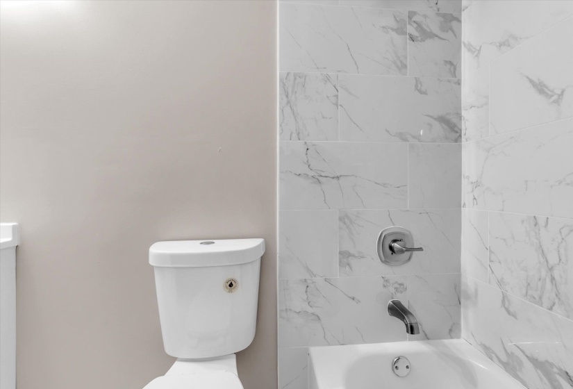 White porcelain bathtub with chrome fixtures and white marble-look subway tile surround