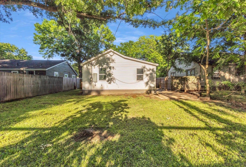 Spacious backyard featuring a manicured lawn, established trees, and a privacy fence