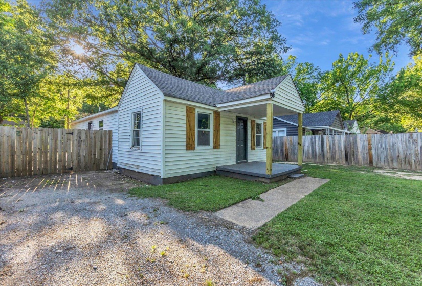 White siding exterior with a covered porch, wood shutters, and a gravel driveway