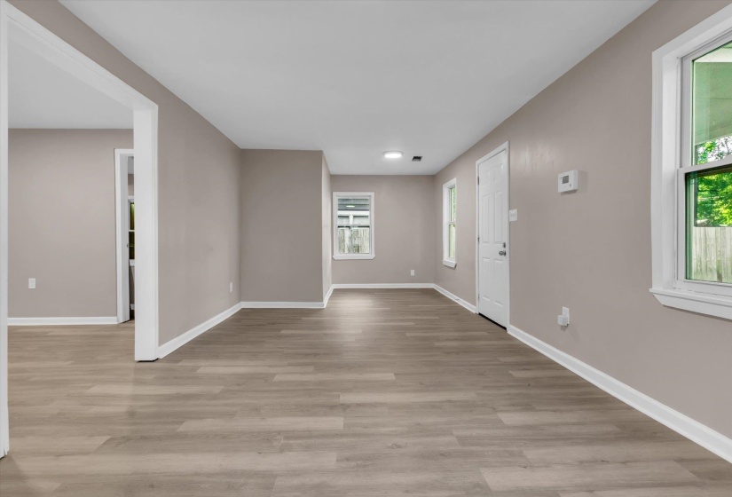 Open living area featuring wood-finish flooring, neutral paint tones, multiple windows, recessed lighting, and white trim throughout