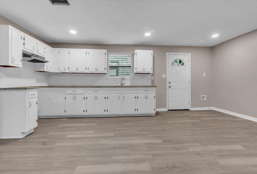 Open-concept living space featuring wood-finish flooring, recessed lighting, and a kitchen with white cabinetry