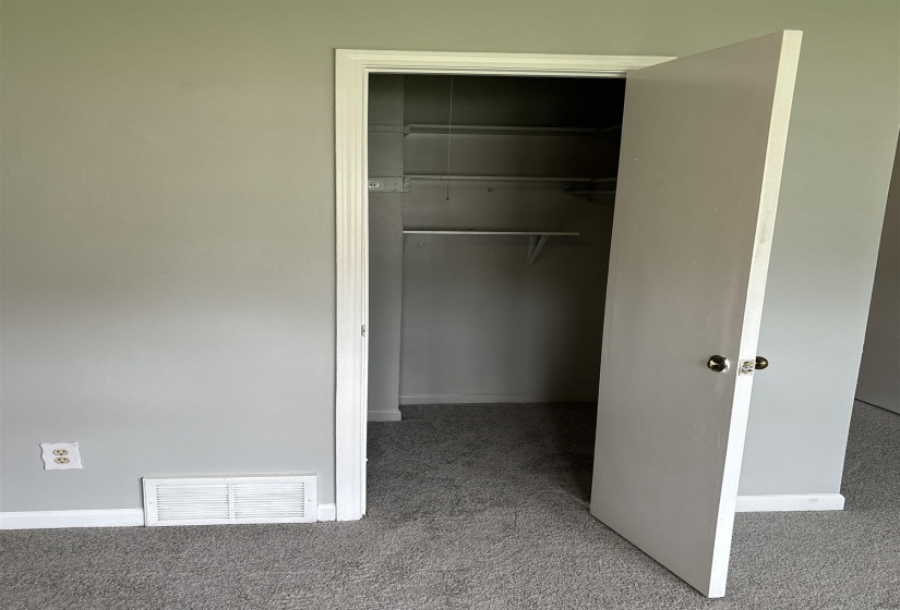 Carpeted interior with light grey walls, a white baseboard, and a white closet door featuring a satin nickel knob