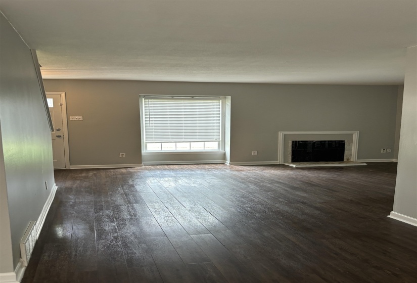 Spacious room featuring wood-finish flooring, a prominent window with blinds, and a decorative fireplace