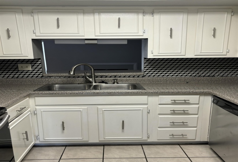 Kitchen area featuring white cabinetry, a double basin stainless steel sink with a gooseneck faucet, speckled countertops, and a patterned backsplash