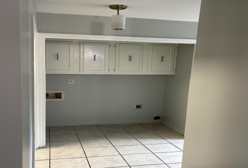 Dedicated laundry area featuring ceramic tile flooring, overhead cabinetry with white finishes, and a contemporary semi-flush mount light fixture