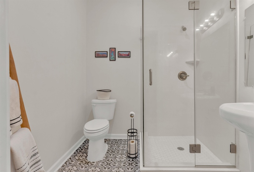 Bathroom featuring a glass-enclosed shower with brushed nickel fixtures, a white toilet, and patterned floor tiling
