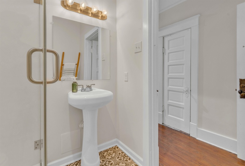 Bathroom featuring a pedestal sink, wall-mounted mirror, and decorative floor tiles